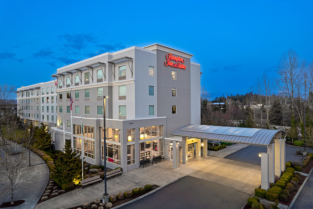 Twilight exterior shot of Hampton Inn & Suites with warm lighting and landscaped entrance